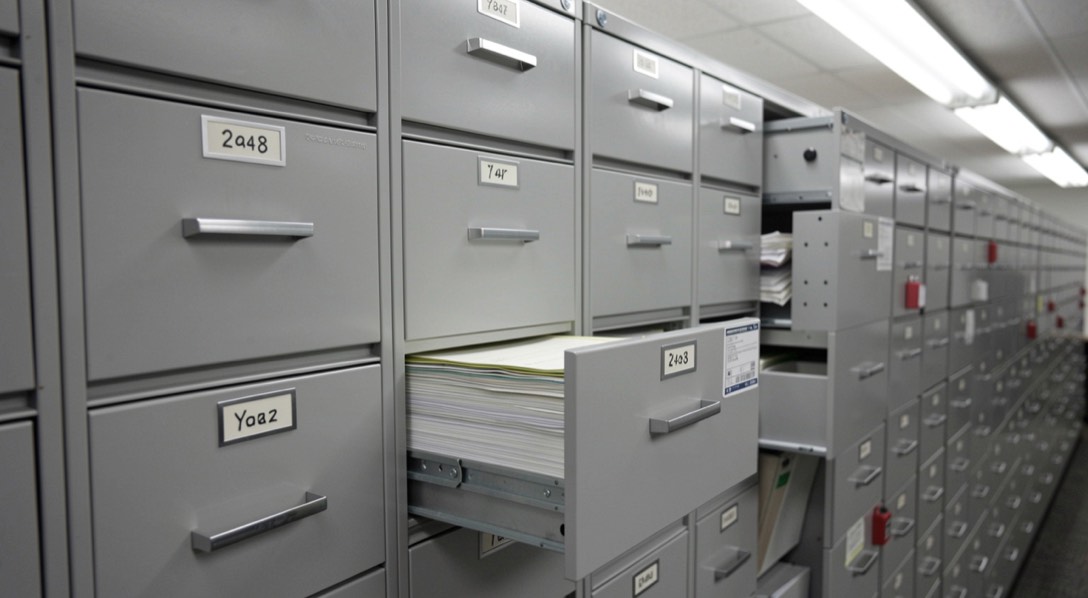 A row of grey filing drawers labelled by year in a records office, one drawer half open
